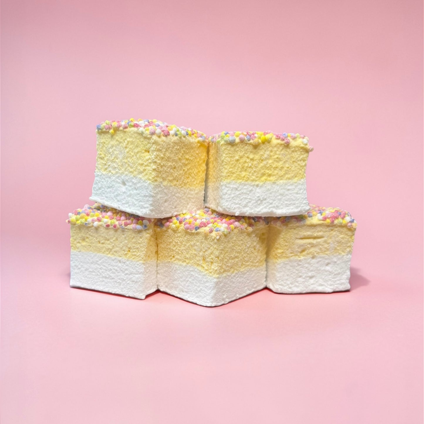 Stack of yellow layered marshmallows with sprinkles on a pink background