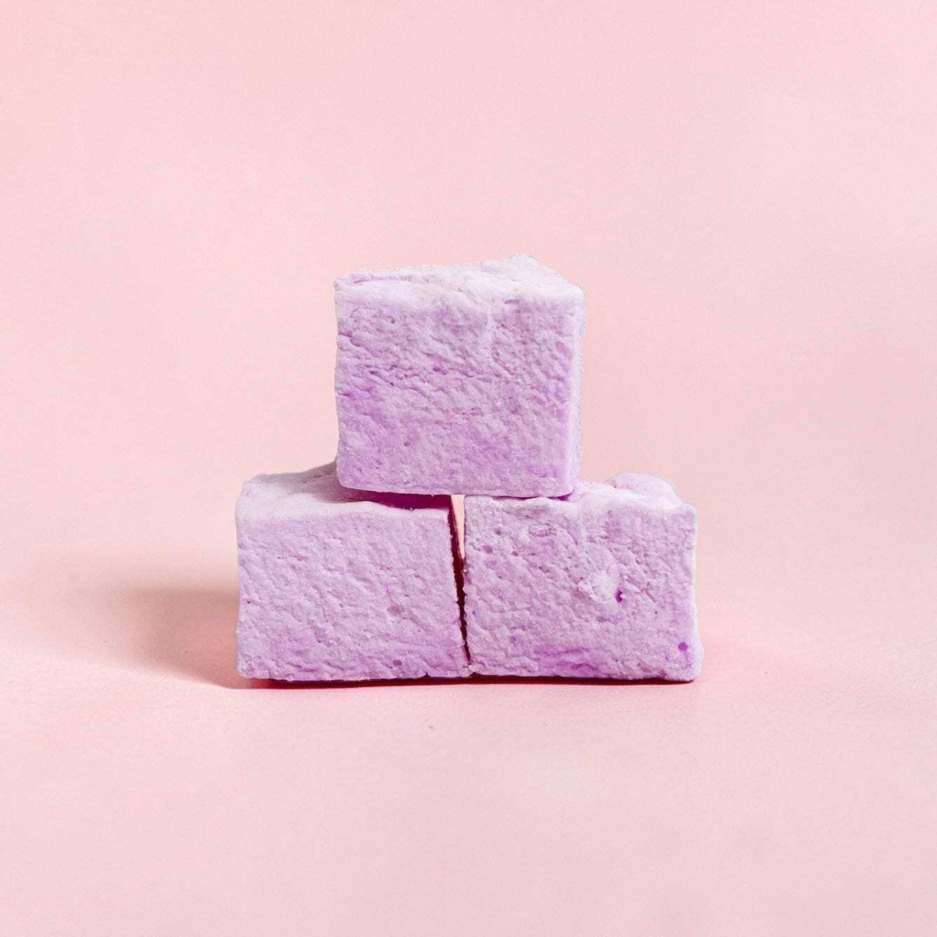 Three purple marshmallows stacked on a light pink background