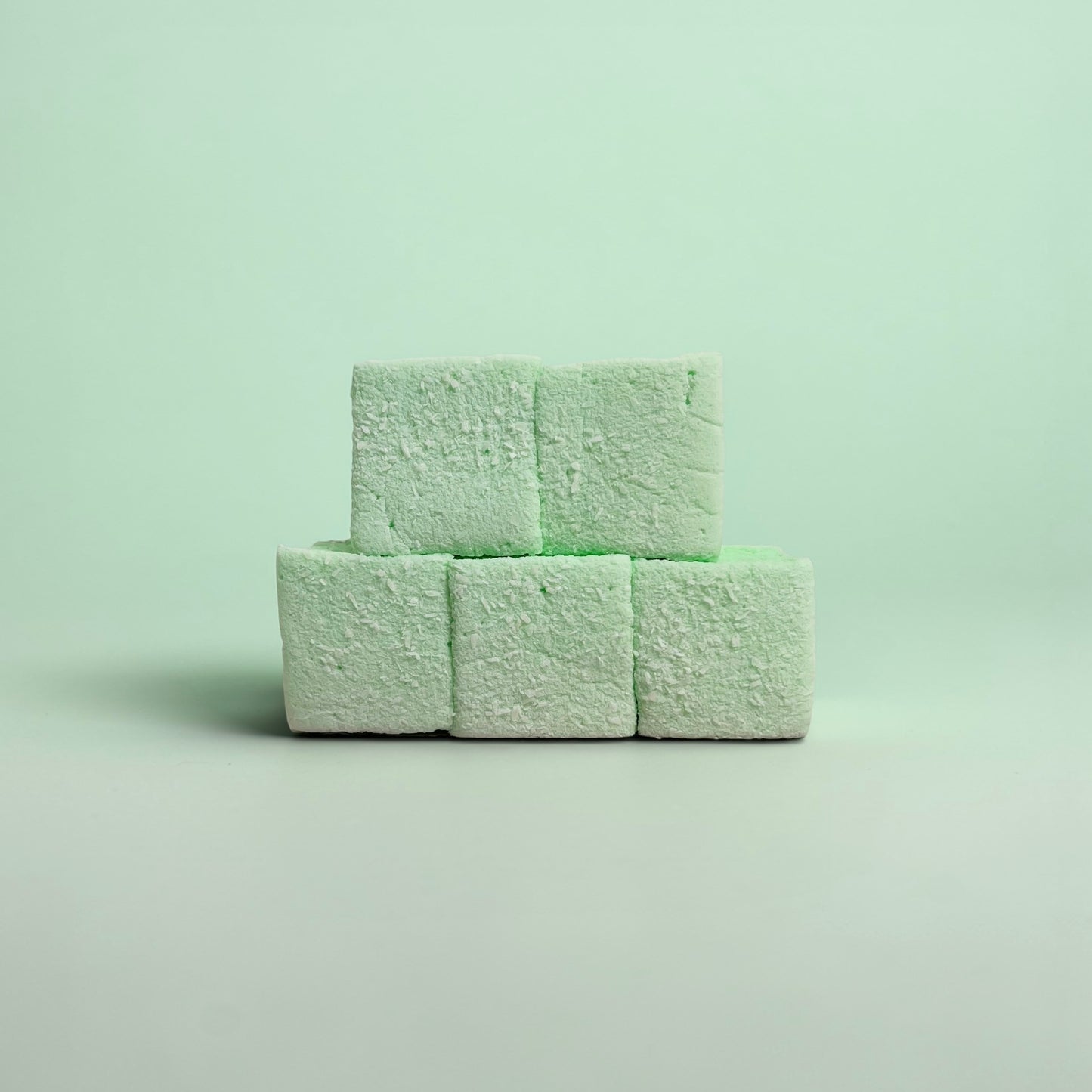 Three green marshmallows stacked on a light green background