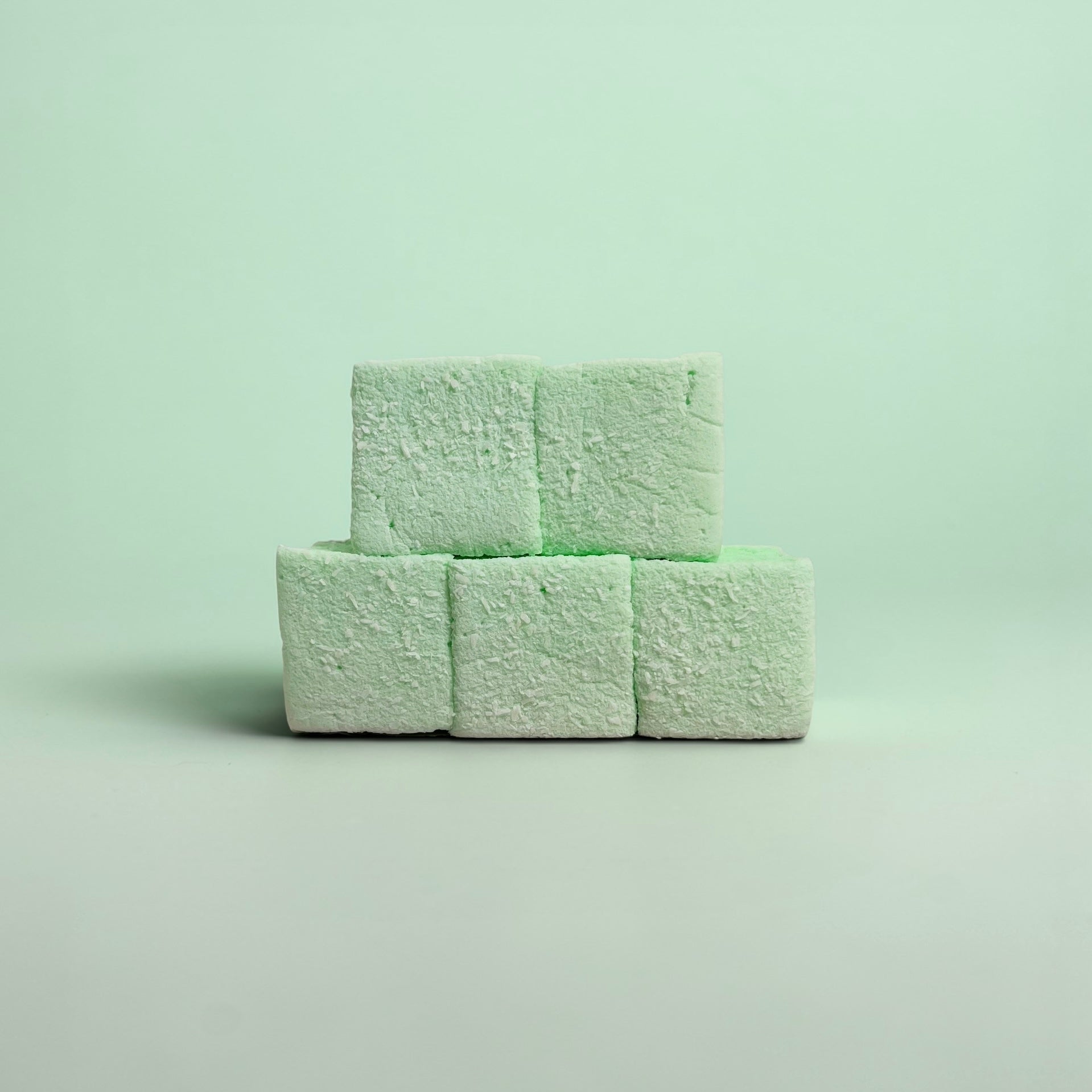 Three green marshmallows stacked on a light green background