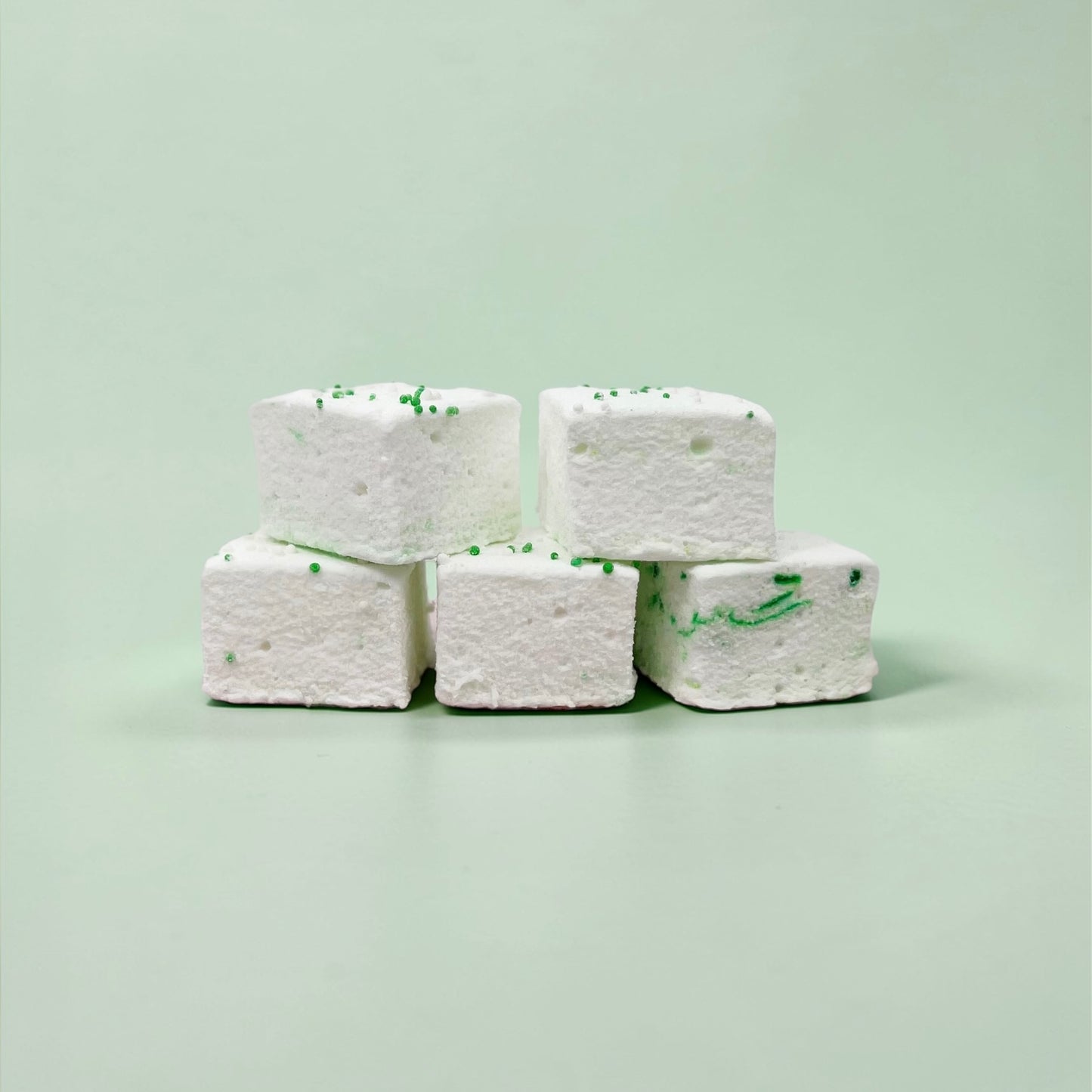 Five white marshmallows with green specks stacked on a light green background