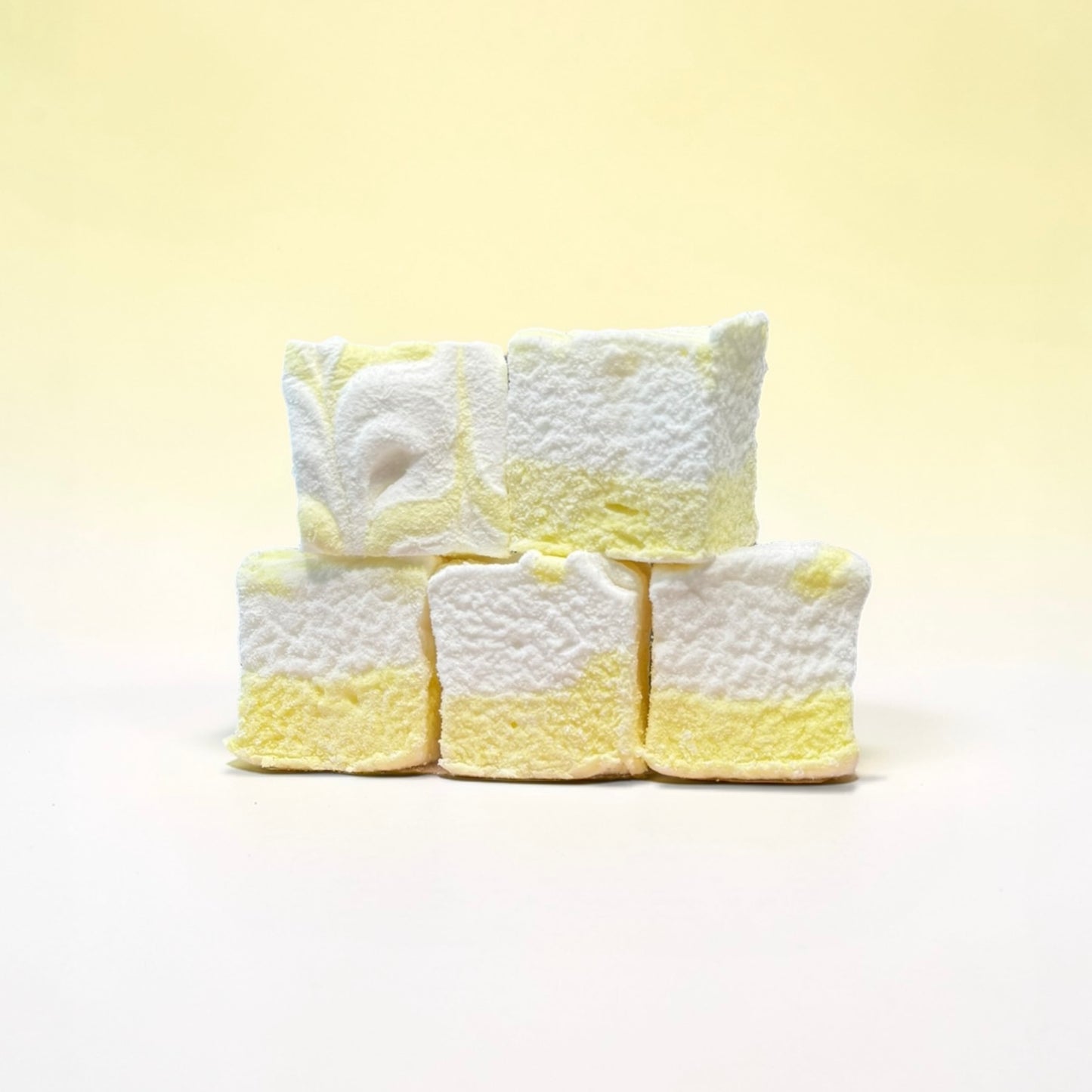 Stack of white and yellow textured marshmallows on a light yellow background