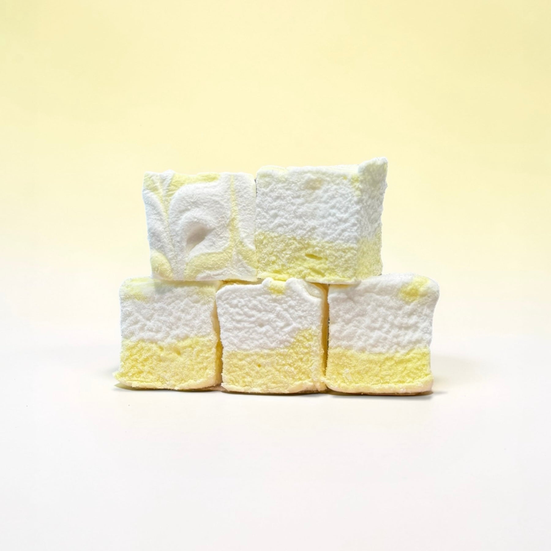 Stack of white and yellow textured marshmallows on a light yellow background