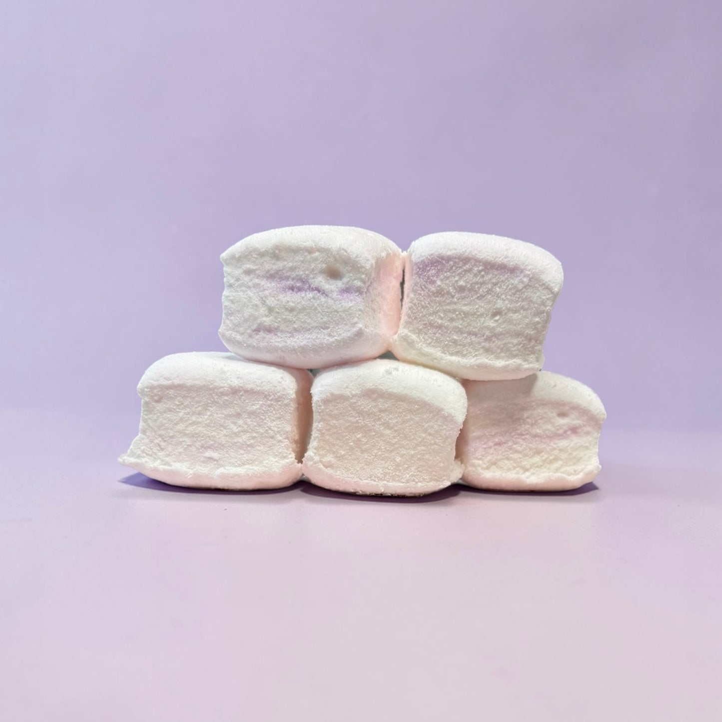 Stack of white marshmallows on a light purple background