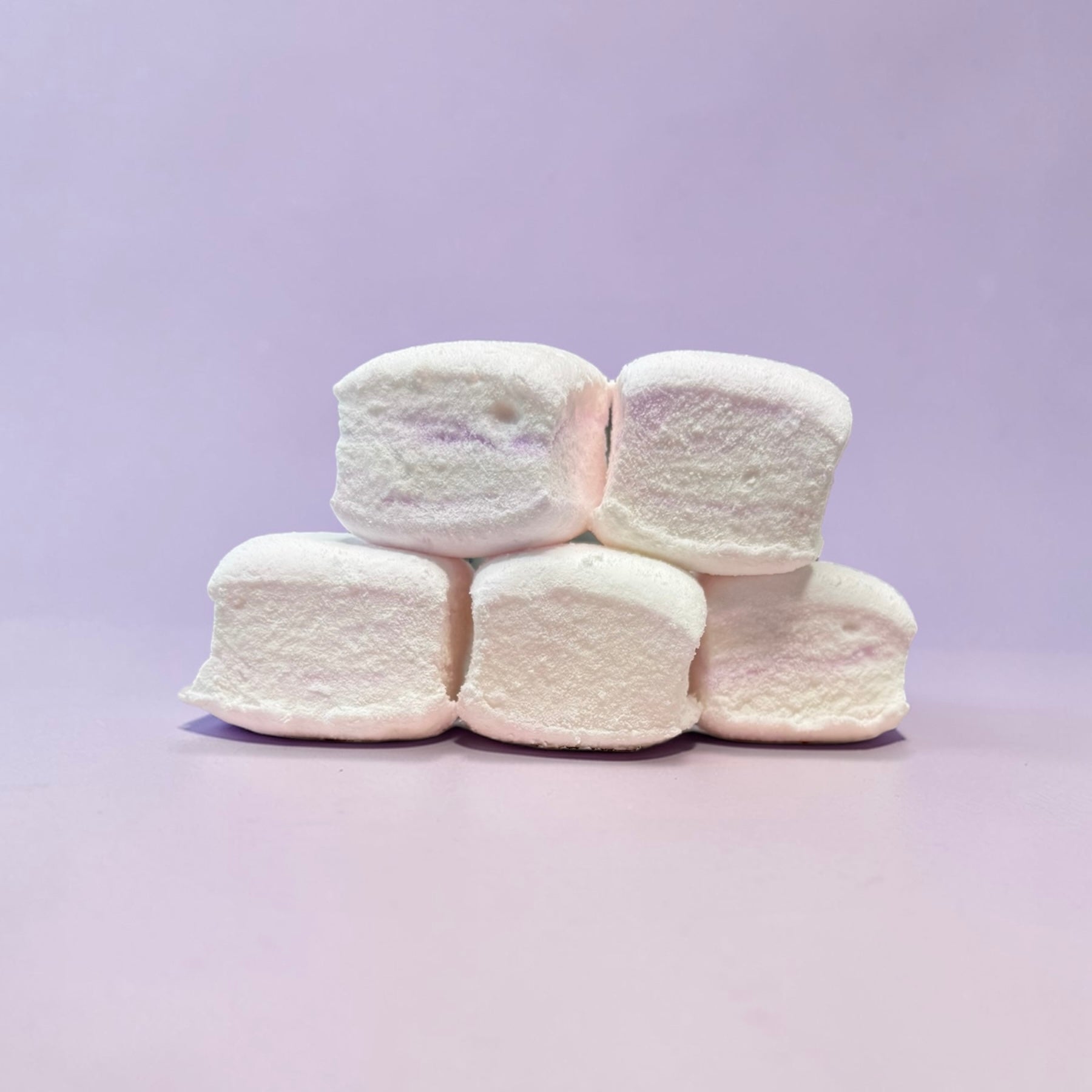 Stack of white marshmallows on a light purple background