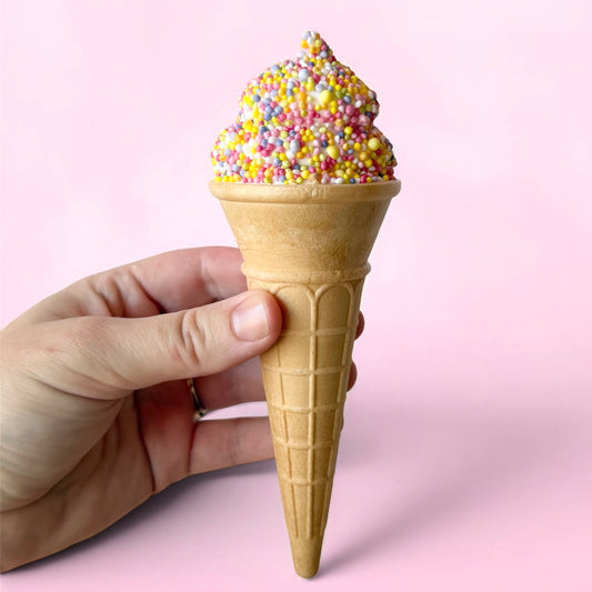Ice cream cone with colorful sprinkles held by a hand against a pink background
