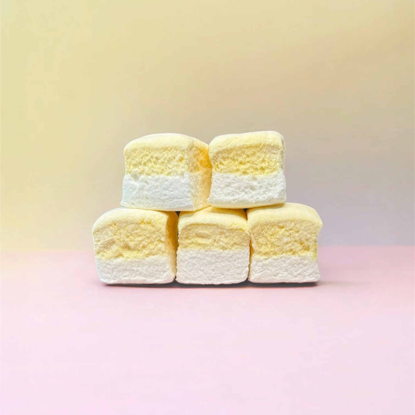 Stack of yellow and white marshmallows on a pink background