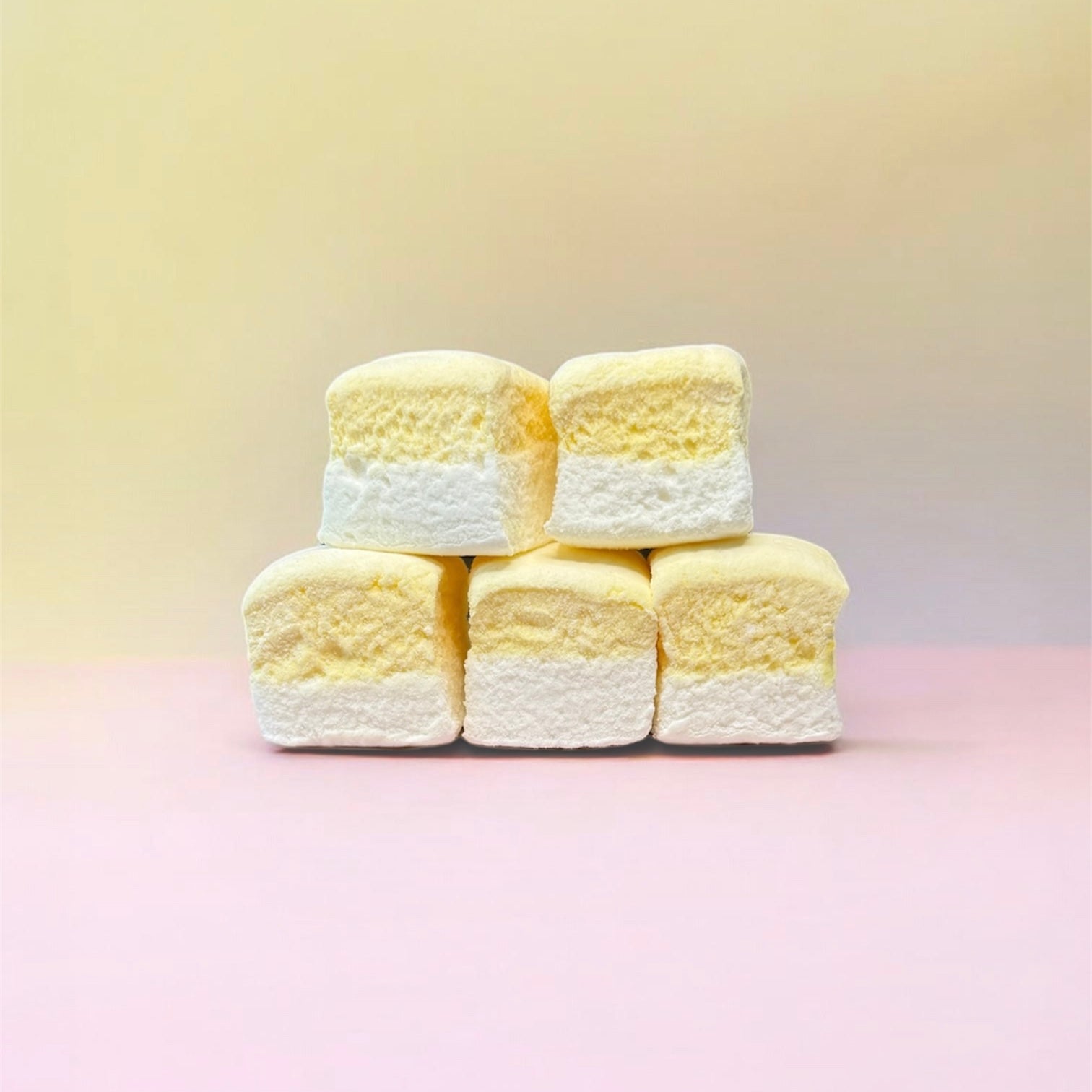 Stack of yellow and white marshmallows on a pink background