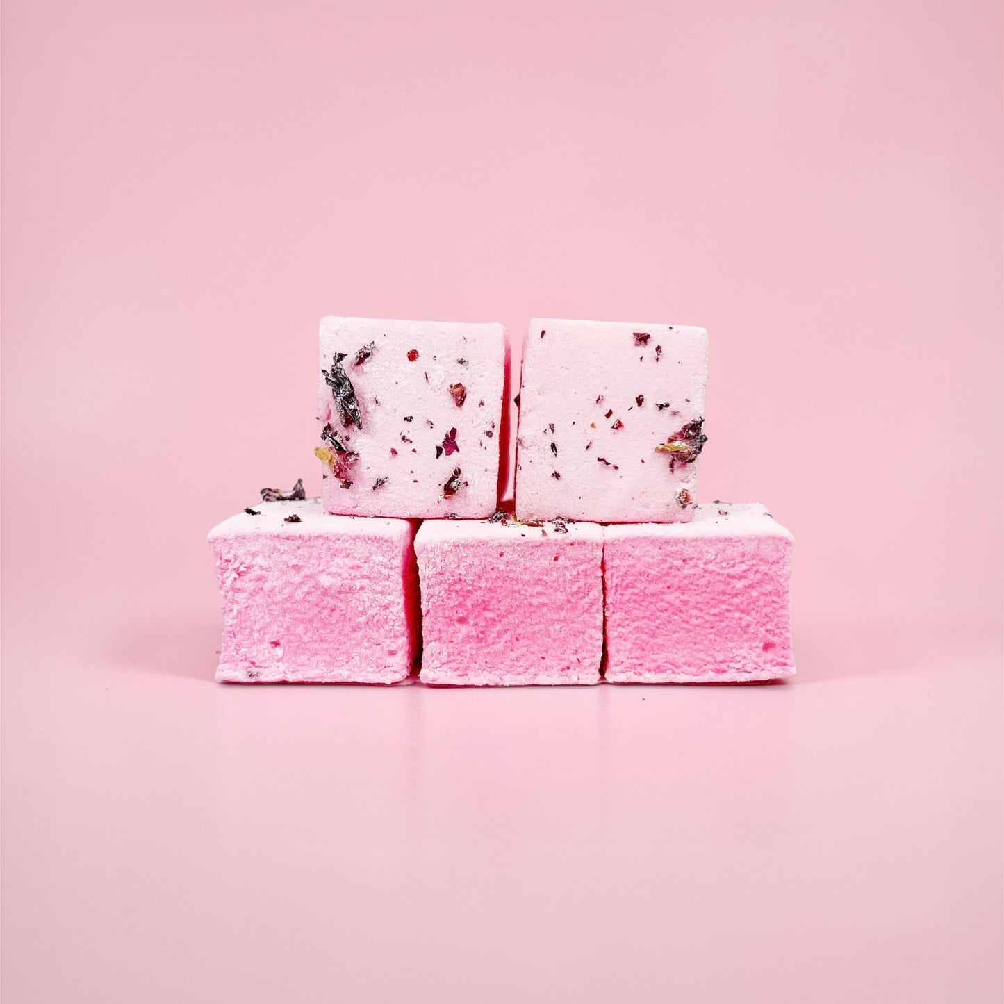 Stack of pink marshmallows with rose petals on a pink background