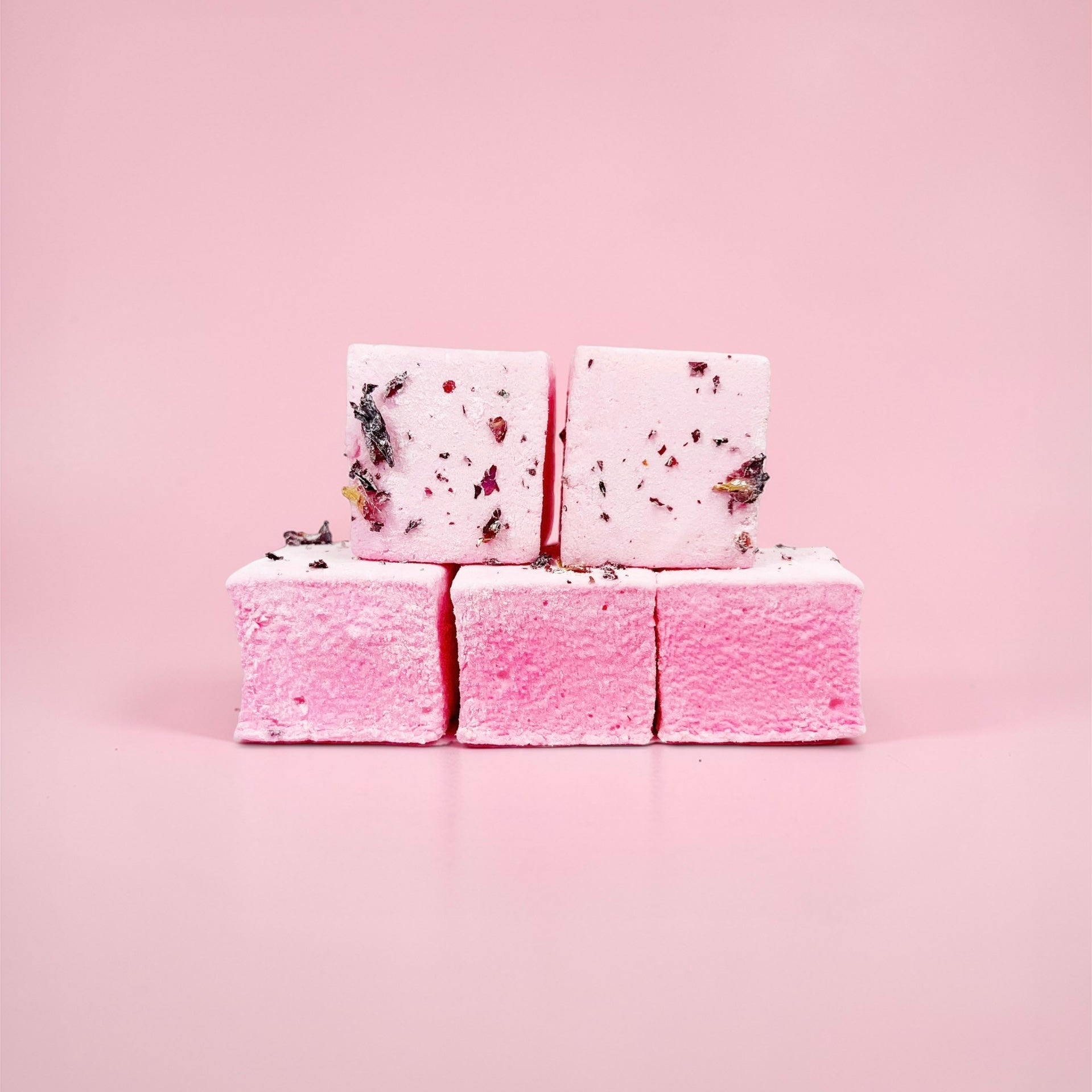 Stack of pink marshmallows with rose petals on a pink background