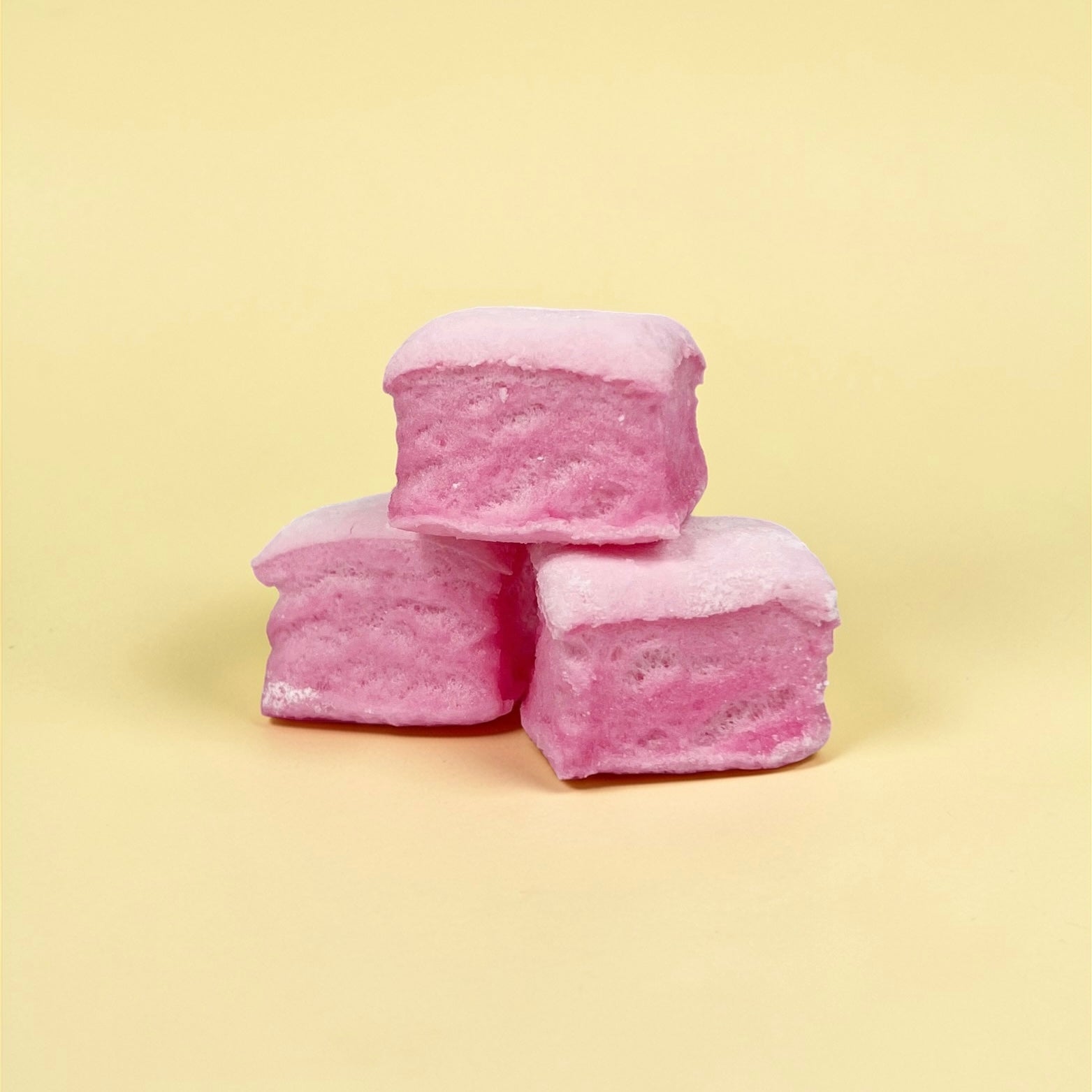 Three pink marshmallows stacked on a light yellow background